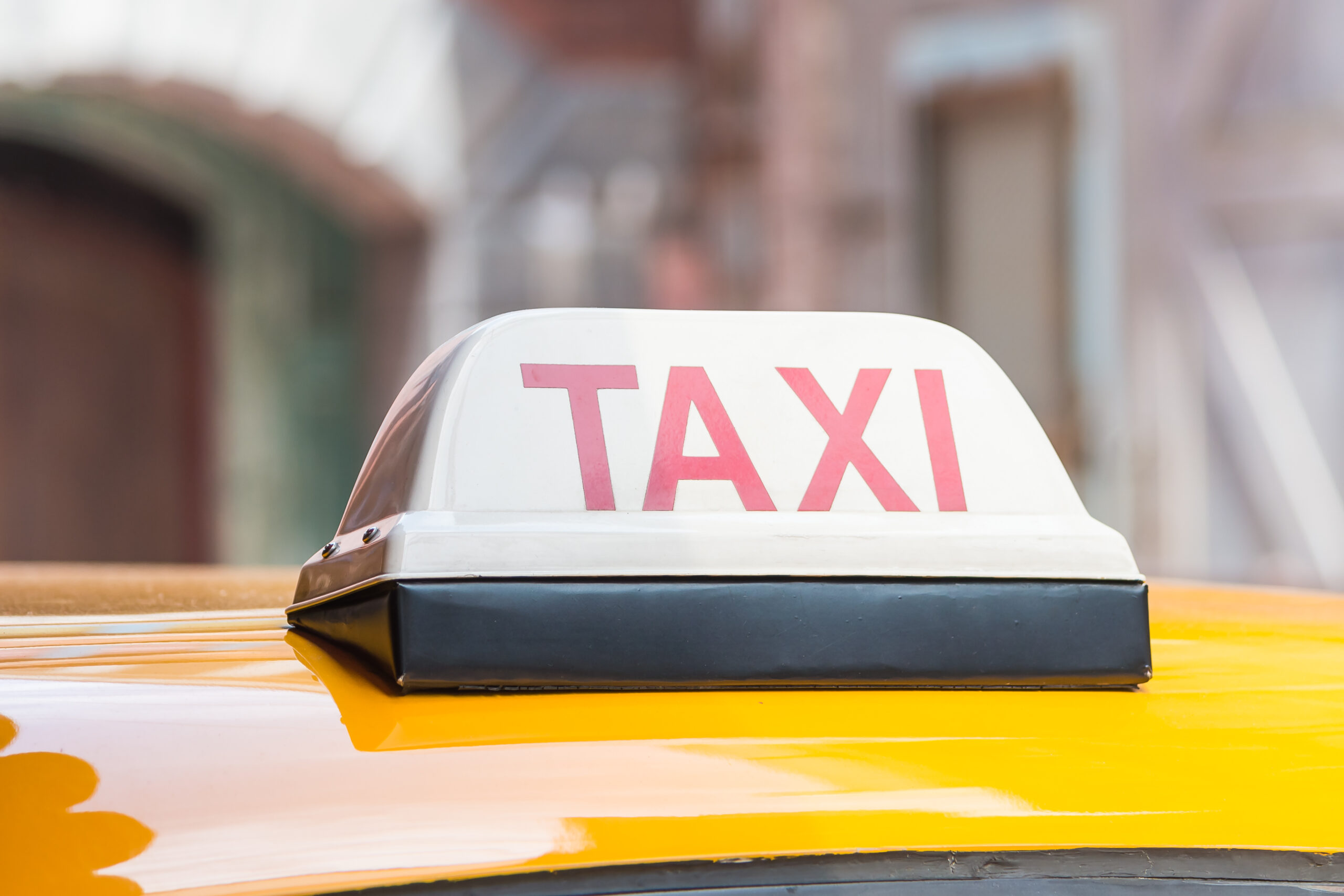 Sarı taksinin tavanında kırmızı harflerle yazılmış TAXI tabelası – Denizli Taksibul şehir içi ulaşım hizmeti.