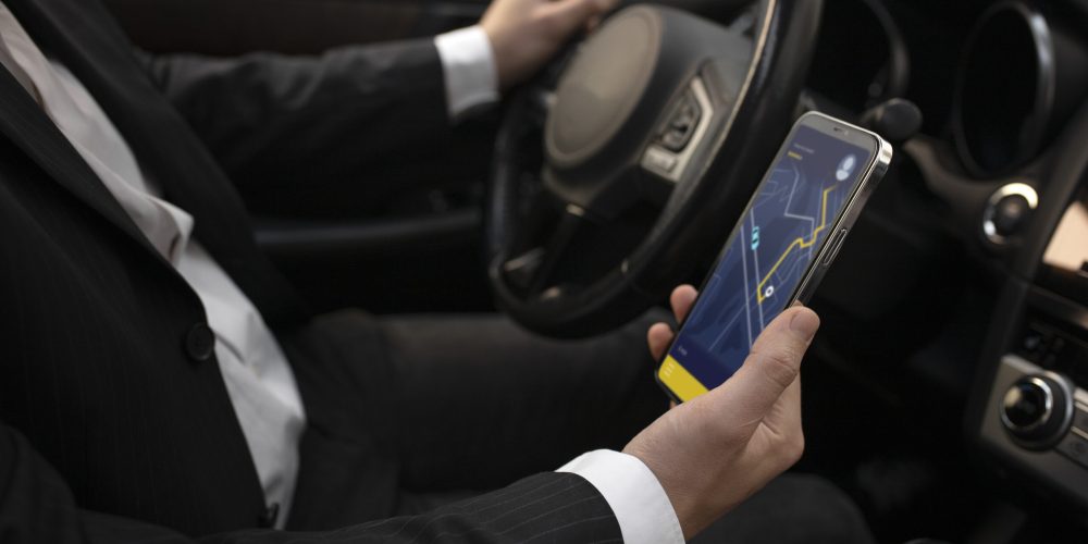 Bir sürücünün araç içinde direksiyonu tutarken diğer eliyle rota gösteren bir navigasyon uygulamasının açık olduğu akıllı telefonu tuttuğu an.