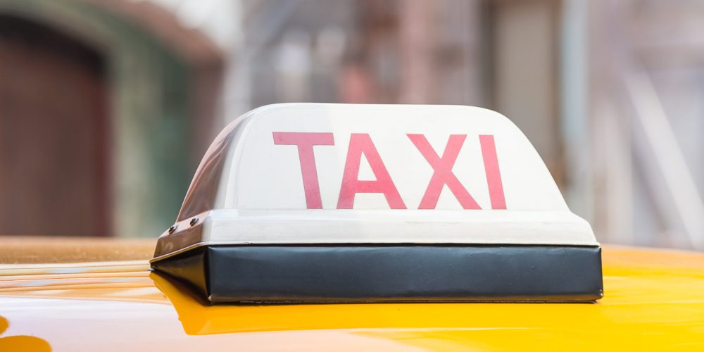 Sarı taksinin tavanında kırmızı harflerle yazılmış TAXI tabelası – Denizli Taksibul şehir içi ulaşım hizmeti.