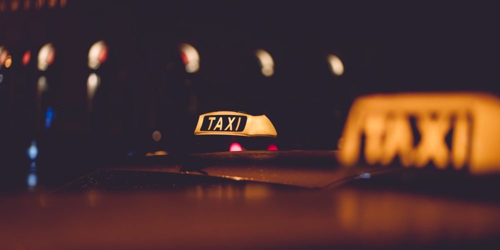 Gece şehir ışıkları arasında sarı taksi tabelası – Denizli Taksibul gece ulaşım hizmeti.